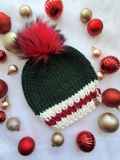 a green and white knitted hat with red pom - pom on top surrounded by christmas ornaments