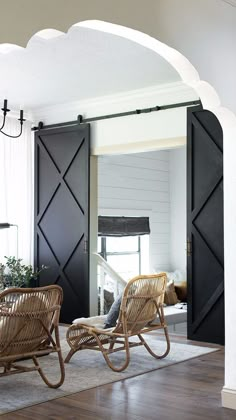 two wicker rocking chairs sit in front of an open door with black shutters