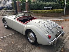 an old white sports car parked in front of a gate