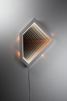 a white square shaped light fixture on a gray wall with a wire running through it