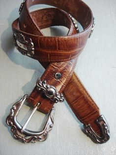 ORNATE CONCHO BELT WITH METAL TIP STRAP LENGTH: 30 1/2 long MADE IN THE USA WIDTH: 1 1/4w MATERIAL: GENUINE LEATHER (DISTRESSED), CROCK EMBOSSED WELL LOVED  BUCKLE: 1 1/4W, 2 1/4H COLOR: BROWN FITS A 24-27 INCH WAIST GOOD-FAIR VINTAGE CONDITION Brown Fits, Concho Belt, Brown Belt, Suspender Belt, Suspenders, Belts, Genuine Leather, Buckle, Leather