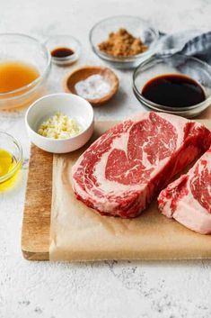 raw steaks on a cutting board with spices and condiments around the meat