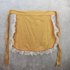 an old yellow apron with ruffled edges on a white background, hanging from the wall