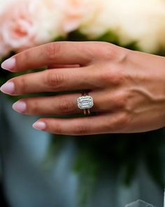 a close up of a person's hand with a ring on their finger and flowers in the background