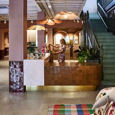 a woman standing at the front desk of a hotel lobby with stairs leading up to it