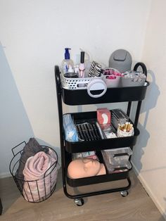 a black cart with lots of items on it next to a white wall and wooden floor