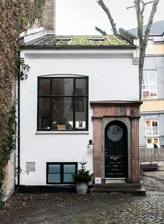 a white house with a black door and window on the side of it, next to a tree