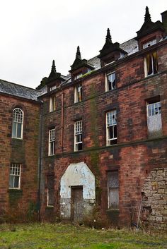 an old brick building with broken windows and no doors on the outside, next to a grassy field