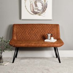 a brown leather couch sitting in front of a painting on the wall next to a potted plant