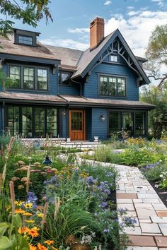 a blue house with lots of windows and flowers in the front yard, surrounded by greenery