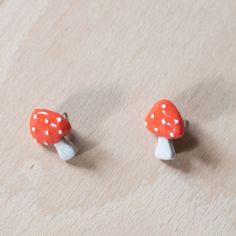 two small red mushrooms sitting on top of a wooden table next to eachother