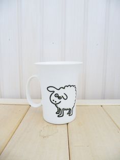 a white coffee cup with a black sheep drawn on the side sitting on a wooden table