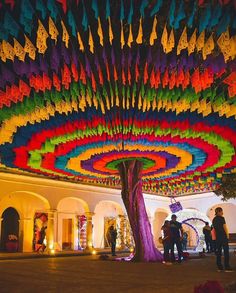 people are standing under a colorfully decorated tree