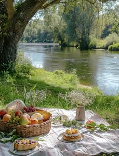 a picnic table with fruit, cheese and bread on it near a riverbank in the background