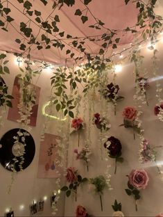 flowers and greenery are hanging from the ceiling in front of a wall with lights