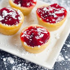 three small pastries on a white plate covered in powdered sugar and cranberry sauce