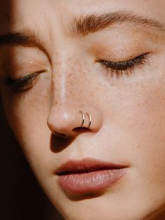 a close up of a person with a nose ring on her nose and eyes closed