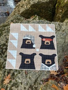 there is a quilt on the rocks with bears in hats and scarfs hanging from it