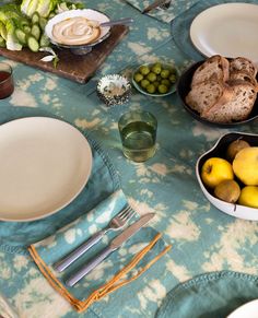 a table topped with plates and bowls filled with food next to utensils on top of a blue cloth covered table