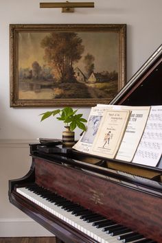 an old piano with music sheets on it in front of a painting and potted plant