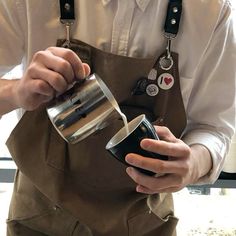 a man in an apron is pouring something into a cup while holding a coffee mug