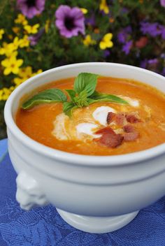 a white bowl filled with soup on top of a blue table cloth next to flowers