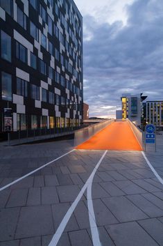 an empty parking lot in front of a tall building with orange lights on the side