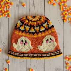 an orange knitted hat with two white birds on it and candy corn scattered around