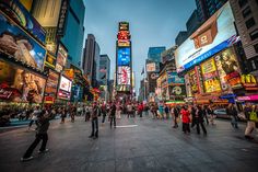 many people are walking around in the city at night, with brightly lit signs and billboards