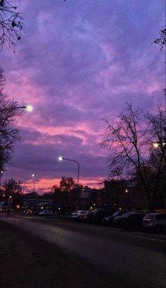 the sky is purple and there are cars parked on the side of the road