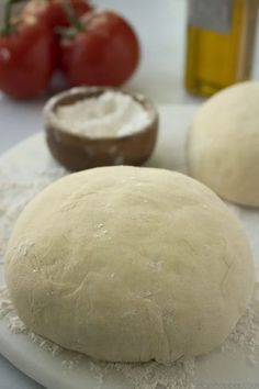 two uncooked breads sitting on top of a cutting board next to tomatoes