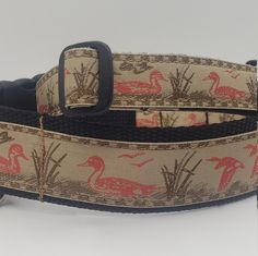 the belt is decorated with birds and reeds on beige fabric, along with a black leather buckle