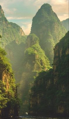 a river surrounded by mountains and greenery in the middle of the day with boats on it