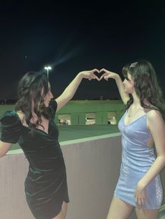 two women standing next to each other holding their hands in the shape of a heart