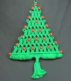 a crocheted christmas tree decoration hanging on a gray background with red balls and tassels