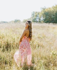 a woman standing in the middle of a field wearing a pink dress and smiling at the camera