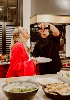 a man and woman standing in front of a counter with food on it while looking at each other