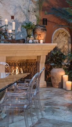 a dining room table and chairs with candles in front of the fire place, surrounded by potted plants