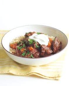 a white bowl filled with meat and rice on top of a yellow towel next to a fork