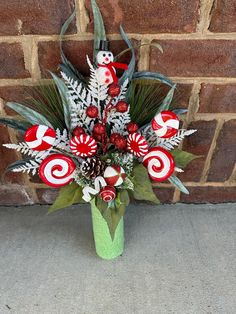 a green vase filled with candy canes and greenery next to a brick wall