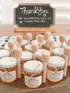 a table topped with lots of honey jars and wooden spoons next to a sign that says thank you for celebrating with us please take one