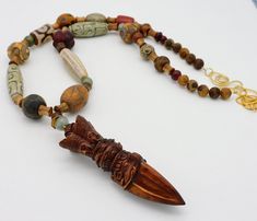 This long, flattering length necklace features an extraordinary handcarved vintage Tibetan boxwood amulet....the workmanship is wonderful!  Amulet is approximately 3 3//4 inches in height and I have topped it with a jade and horn bead.  Amulet hangs from long necklace made of a plethora of stunning handcarved beads....including etched and handpainted Tibetan agate in various shapes, sizes and colors, jade, gorgeous handcarved high-quality horn beads, handcarved wooden spacer beads from Vietnam and handmade Mprccan bead. Necklace fastens with my signature, large fancy handmade brass clasp and high-quality 18KT matte gold over brass chain.  Chain is tarnish-resistant.   Length adjusts from about 27 -29 inches. Brown Carved Amulet Necklaces, Carved Beaded Necklaces For Spiritual Gifts, Spiritual Carved Beaded Necklace As Gift, Spiritual Carved Beaded Necklace For Gift, Unique Brown Jewelry For Ceremonial Occasions, Artisan Carved Necklace For Collectors, Artisan Carved Necklace Collectible, Traditional Brown Carved Jewelry, Unique Carved Beaded Necklaces As Gift