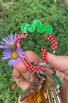 a person holding several keys in front of a purple flower and green plant with polka dots on it