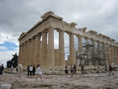 many people are walking around in front of the parthenion on a cloudy day