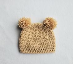 a crocheted hat with two pom - poms sits on a white surface