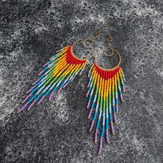 a pair of multicolored beaded earrings sitting on top of a gray surface