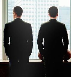 two men standing next to each other in front of a window looking out at the city