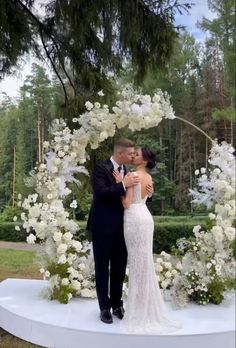 a bride and groom are standing under an arch with white flowers on it at their wedding