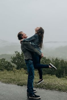 a man holding a woman in his arms while standing on the side of a road