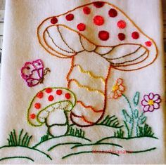 a close up of a piece of embroidery on a cloth with flowers and mushrooms in the background